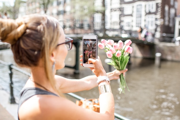 Foto jonge vrouw fotografeert met telefoon mooi boeket roze tulpen op de achtergrond van de stad in amsterdam