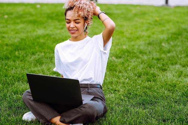 Jonge vrouw freelancer geniet van het kijken naar educatieve webinar op laptop zittend op groen gras