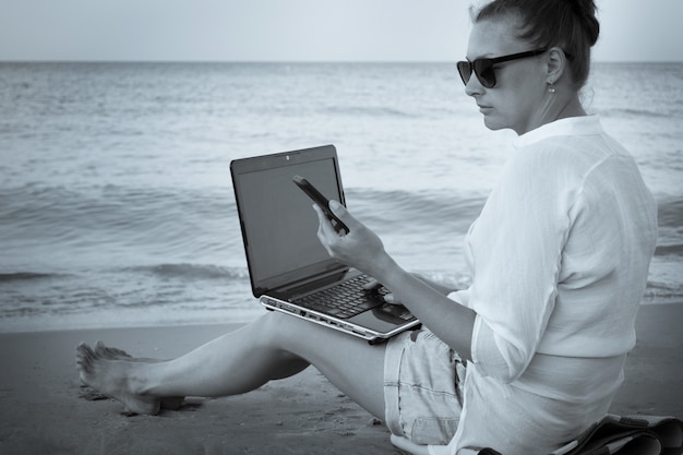 jonge vrouw freelancer werkt aan de kust. vrouw met laptopcomputer op het strand, zwart-wit foto. Freelance werk, vakantie