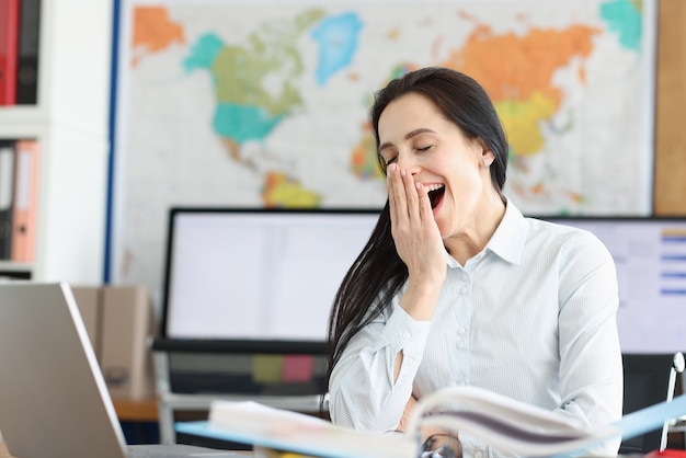 Jonge vrouw gaapt op werkplek voor laptop