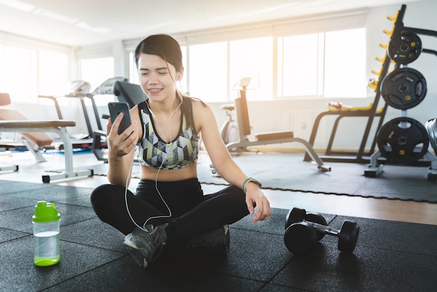 Foto jonge vrouw gebruikend smartphone en luisterend muziek met oortelefoons terwijl het nemen van onderbreking na training in gymnastiek