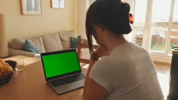 Jonge vrouw gebruikt laptop groen scherm Chromakey terwijl ze in een appartement zit