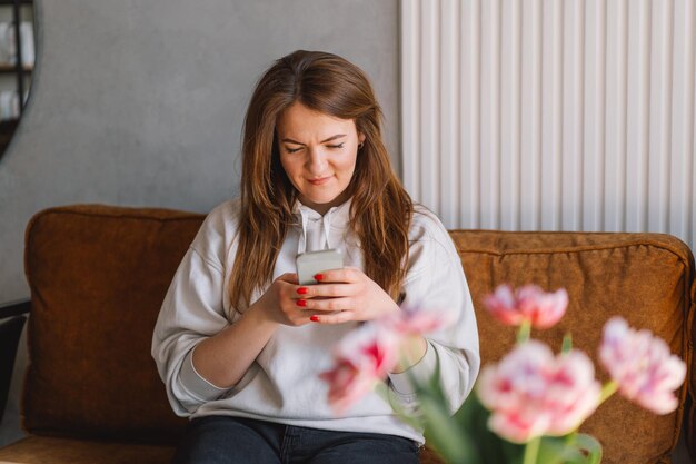 Jonge vrouw gebruikt mobiele telefoon Drink koffie en zit alleen aan tafel in de coffeeshop