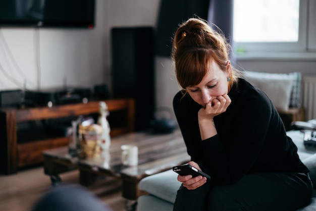 Jonge vrouw gebruikt telefoon terwijl ze thuis op de bank zit