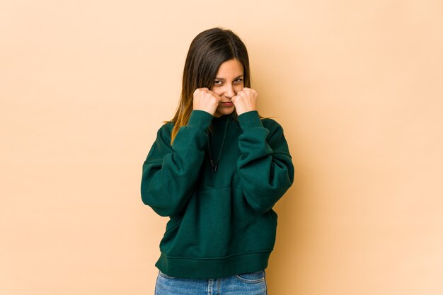 Jonge vrouw geïsoleerd op beige achtergrond een klap, woede gooien, vechten als gevolg van een argument, boksen.