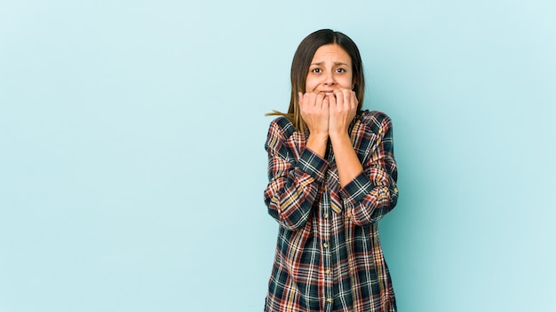 Jonge vrouw geïsoleerd op blauwe achtergrond vingernagels bijten, nerveus en erg angstig.