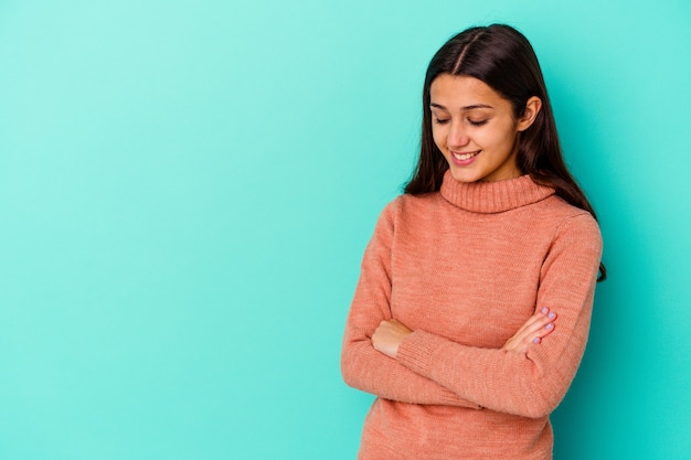 Jonge vrouw geïsoleerd op blauwe muur glimlachend zelfverzekerd met gekruiste armen