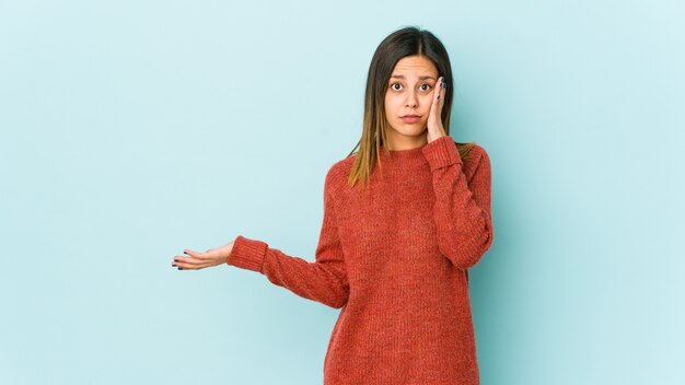 Jonge vrouw geïsoleerd op blauwe muur onder de indruk kopie ruimte op palm te houden.