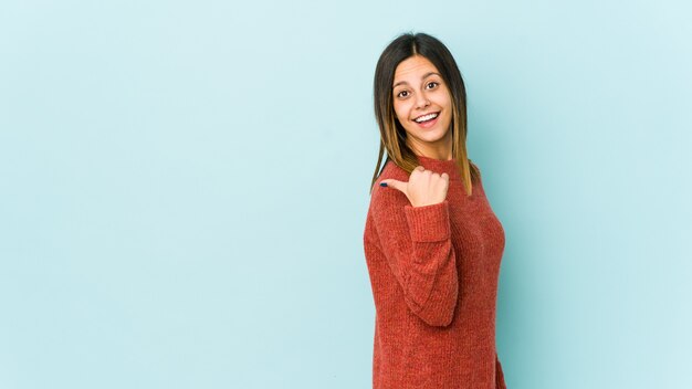 Jonge vrouw geïsoleerd op blauwe punten met duimvinger weg, lachend en zorgeloos.