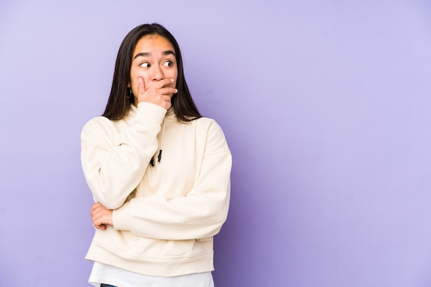 Jonge vrouw geïsoleerd op een paarse doordachte op zoek naar een kopie ruimte die mond bedekt met hand.