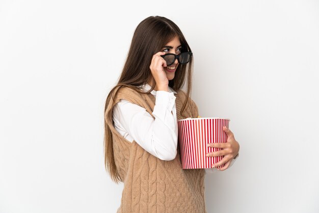 Jonge vrouw geïsoleerd op een witte muur met 3d-bril en met een grote emmer popcorn