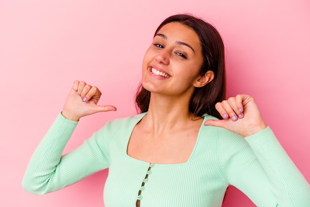 Jonge vrouw geïsoleerd op roze muur voelt zich trots en zelfverzekerd, voorbeeld om te volgen