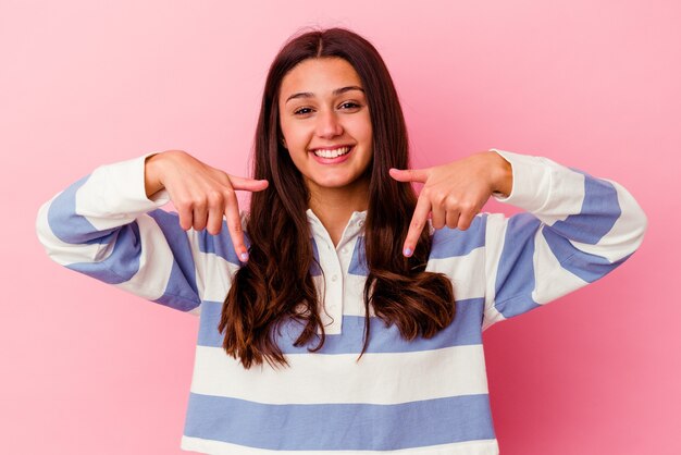 Jonge vrouw geïsoleerd op roze muur wijst naar beneden met vingers, positief gevoel