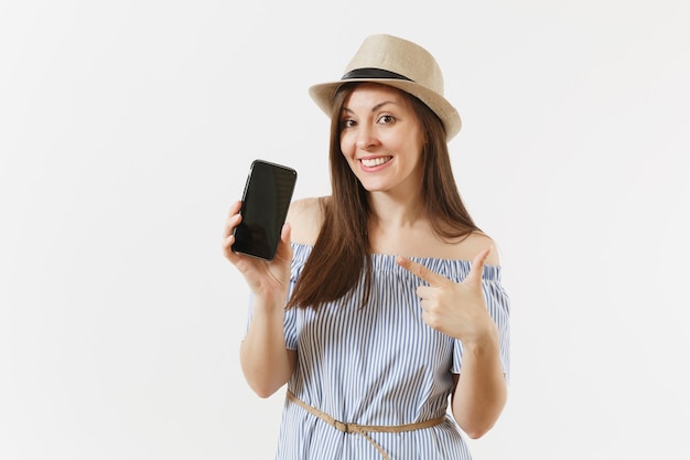 Jonge vrouw gekleed blauwe jurk, hoed weergegeven: camera mobiele telefoon met leeg zwart leeg scherm geïsoleerd op een witte achtergrond. Mensen oprechte emoties, lifestyle concept. Reclame gebied. Ruimte kopiëren.