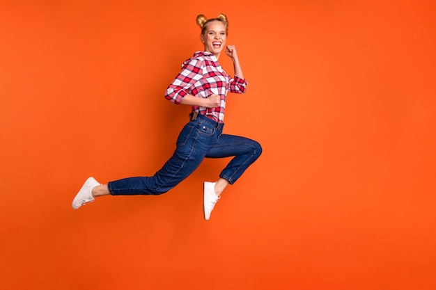 jonge vrouw gekleed in een geruite geruit overhemd springen en poseren geïsoleerd op oranje