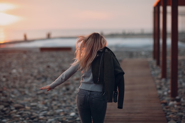 Jonge vrouw gekleed in jeans en trui op het kiezelstrand aan de kust.