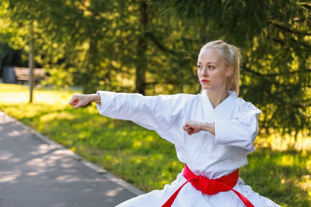 Jonge vrouw gekleed in kimono beoefenen van haar karatebewegingen in park - rode gordel