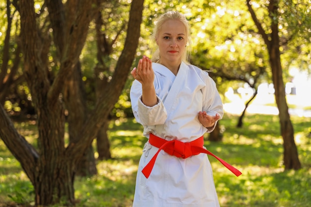 Jonge vrouw gekleed in kimono beoefenen van haar karatebewegingen in park - rode gordel