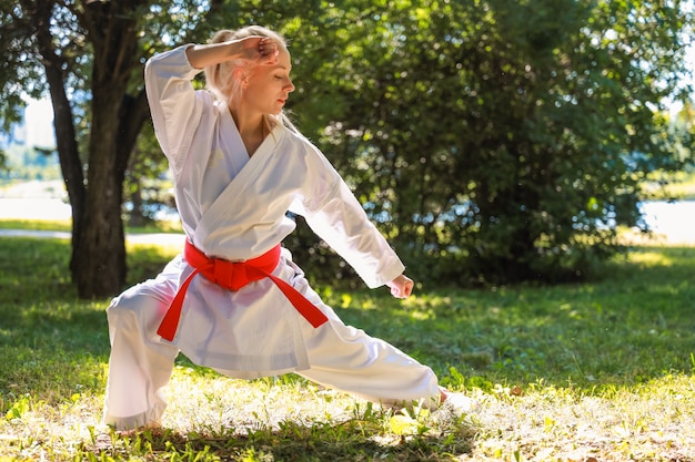 Jonge vrouw gekleed in kimono beoefenen van haar karatebewegingen in park - rode gordel