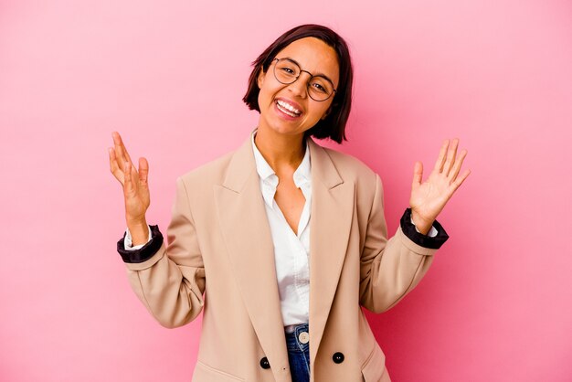 Jonge vrouw gemengd ras bedrijf geïsoleerd op roze achtergrond een overwinning of succes vieren, hij is verrast en geschokt.