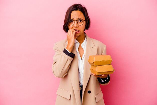 Jonge vrouw gemengd ras bedrijf geïsoleerd op roze achtergrond nagels bijten, nerveus en erg angstig.