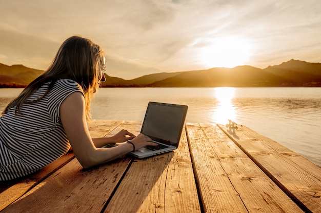 jonge vrouw geniet van haar creativiteit boek schrijven op een pier bij zonsondergang. nieuwe baan kans