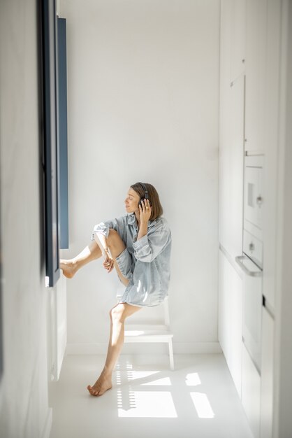 Jonge vrouw geniet van muziek in een koptelefoon terwijl ze alleen in een lichte kamer thuis zit. Zelfisolatie en eenzaamheid concept