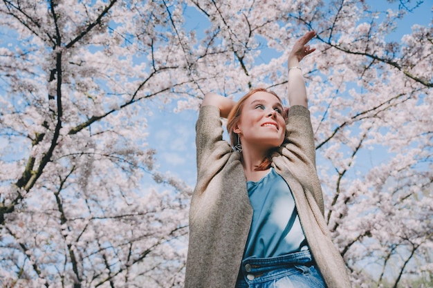 Jonge vrouw genieten van de natuur in het voorjaar picknick met glas wijn onder kersenbloesembomen vrouw genieten van het leven en een prachtig park met kersenbomen in bloei geluk concept