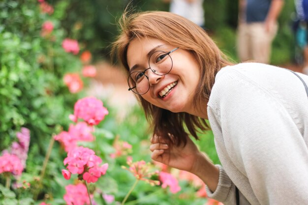 Foto jonge vrouw glimlacht terwijl ze bij bloeiende planten staat