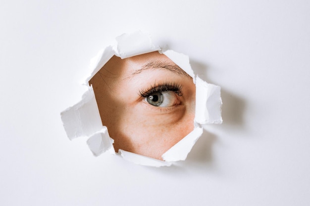 Foto jonge vrouw gluurt door een gat in een papieren witte muur