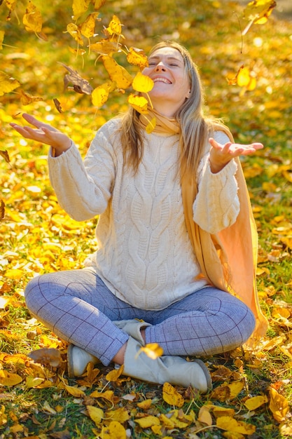 Jonge vrouw gooit bladeren in een park in de herfst