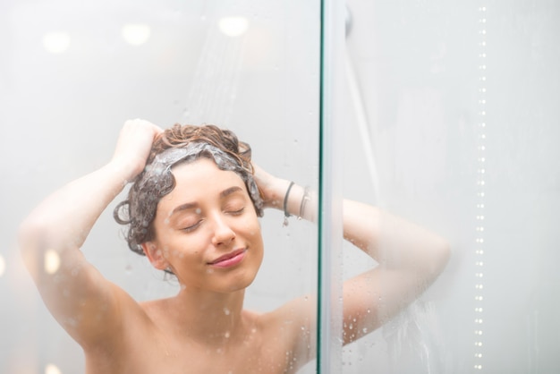 Jonge vrouw haar wassen met shanpoo in de douche. Haarverzorging