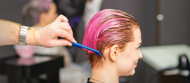 Foto jonge vrouw haarbehandeling na roze kleuren met de hand van mannelijke kapper in kapsalon