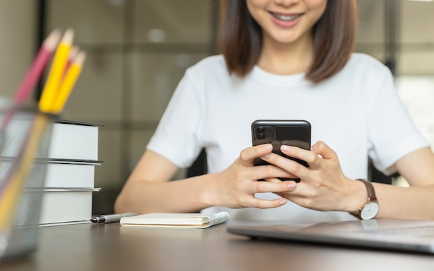 Jonge vrouw hand met smartphone en chatten met vrienden op sociaal netwerk op tafel.