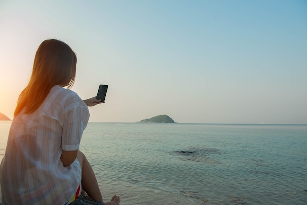 Jonge vrouw handen gebruiken smartphone zittend op een rots genietend van het strand