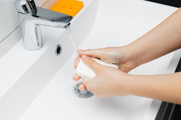 Jonge vrouw handen wassen onder stromend water uit kraan met zeep in badkamer hygiëne concept