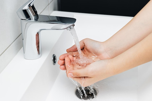 Jonge vrouw handen wassen onder stromend water uit kraan zonder zeep in badkamer hygiëne concept
