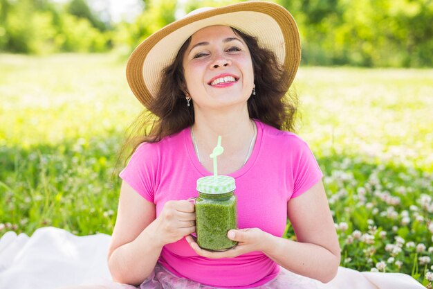 Jonge vrouw heeft plezier in het park en drink groene smoothies tijdens een picknick.