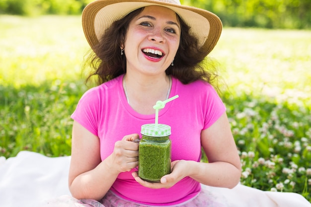 Jonge vrouw heeft plezier in het park en drink groene smoothies tijdens een picknick.