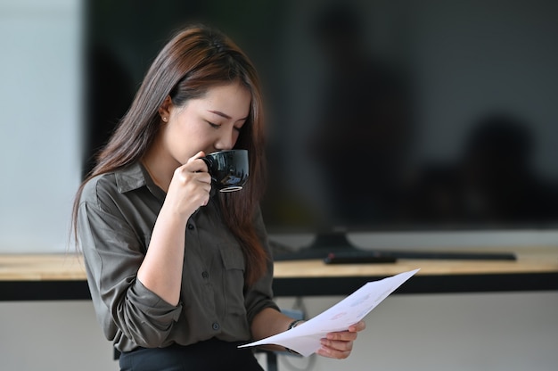 Jonge vrouw het drinken koffie en analyse financieel document.
