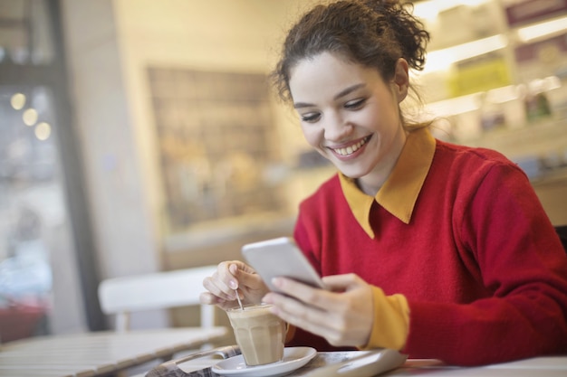 Jonge vrouw het drinken koffie en het controleren van haar telefoon