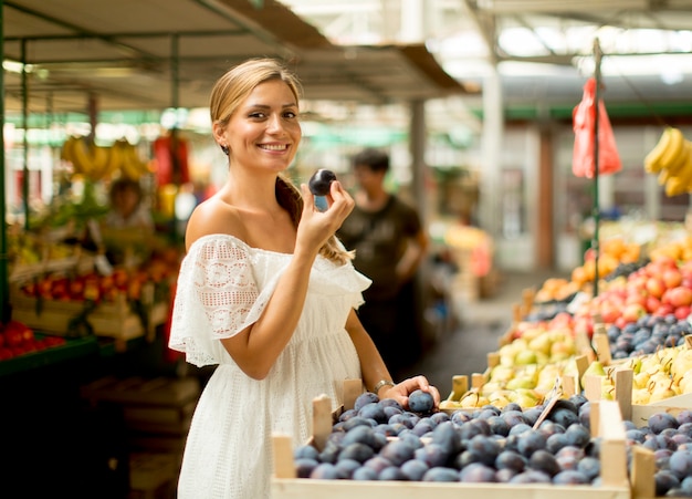 Jonge vrouw het kopen van pruimen op de markt