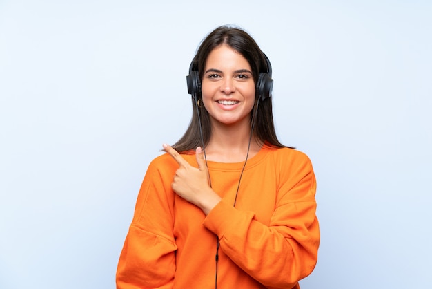 Jonge vrouw het luisteren muziek met mobiel over geïsoleerde blauwe muur die aan de kant richt om een product te presenteren