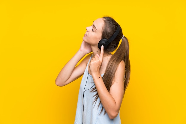 Jonge vrouw het luisteren muziek over geïsoleerde gele muur