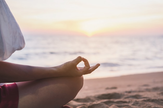 Jonge vrouw het praktizeren yoga op het tropische strand bij zonsondergang