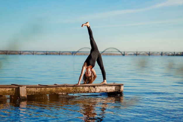 Jonge vrouw het praktizeren yogaoefening bij stille houten pijler met stadsachtergrond. Sport en recreatie in de stad