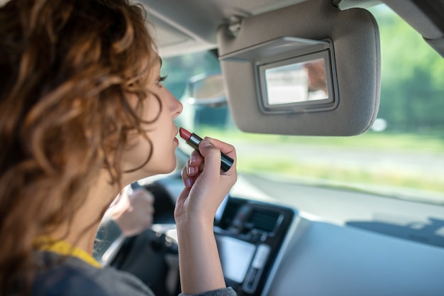 Jonge vrouw het schilderen lippen in een auto