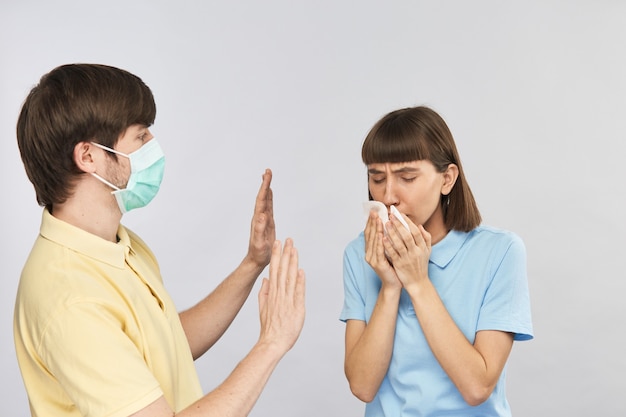 Jonge vrouw hoesten aan servet en man in gasmasker schoen afstand van haar houden, afstand houden terwijl corovirus