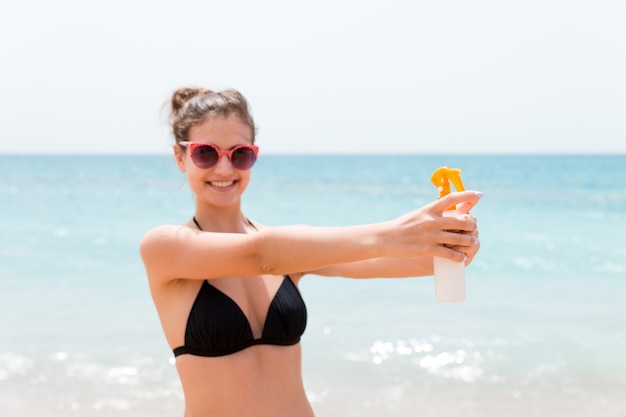 Jonge vrouw houdt een fles sunblock voor lichaam op de achtergrond van de zee.