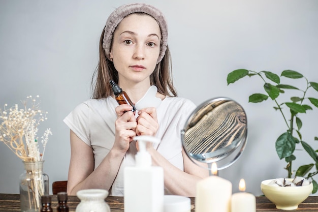 Jonge vrouw houdt een gouache schraper stimulator en een fles natuurlijke biologische olie voor massage en huidverzorging Er is een aromalamp met etherische oliën kaarsen op tafel